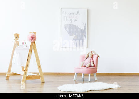 Butterfly poster, wooden clothes hanger and pink armchair with a rabbit in a kid room interior Stock Photo