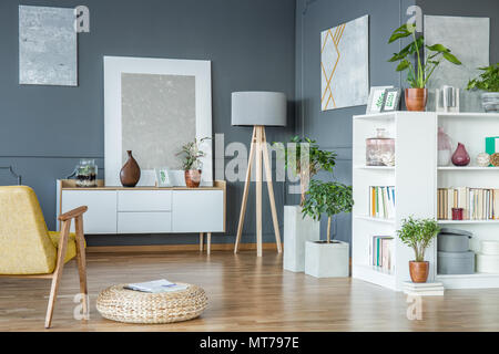 Wooden lamp placed in the corner of living room interior with fresh potted plants, gallery and books Stock Photo