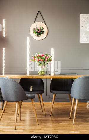 Tulips poster hanging on the wall and fresh flowers in vase placed on wooden table in grey dining room interior Stock Photo