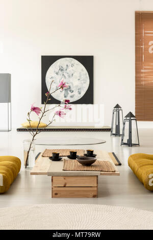 Cherry blossom in a Japanese living room interior with a painting, coffee table with cups and yellow pillows on the floor Stock Photo