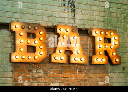 Bar signboard. Inscription from large metal letters decorated with glowing light bulbs on the brick wall Stock Photo