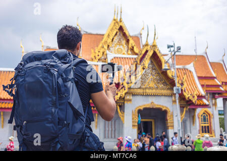 Man backpacher who holds mobile phone on gimbal visiting Asia during a sunny day , Solo trip , holiday and vacations concept . Stock Photo