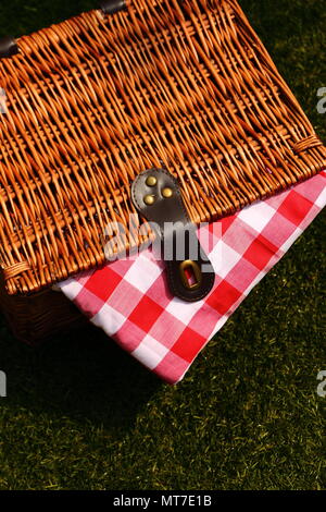 Wicker picnic basket with a red and white gingham cloth on a grass background Stock Photo