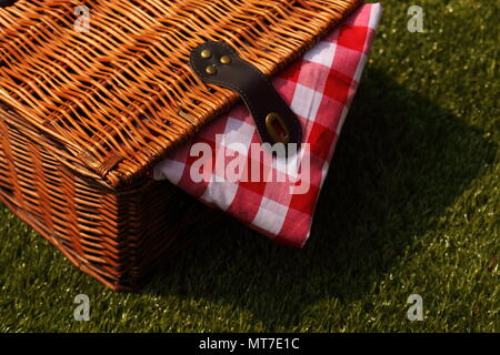 Wicker picnic basket with a red and white gingham cloth on a grass background Stock Photo