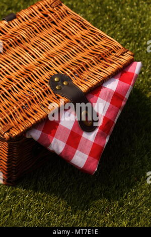 Wicker picnic basket with a red and white gingham cloth on a grass background Stock Photo