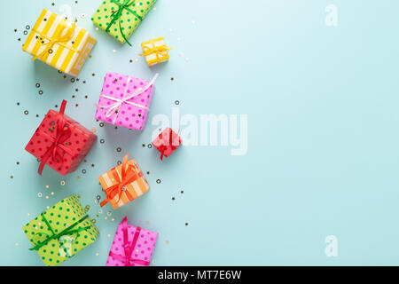 Holiday flat lay with gift boxes wrapped in colorful paper and tied with bows on blue background, decorated with confetti. Birthday, Christmas and sal Stock Photo