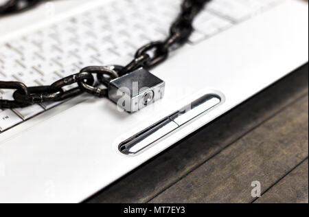Heavy chain with a padlock around a laptop on gray table. Stock Photo