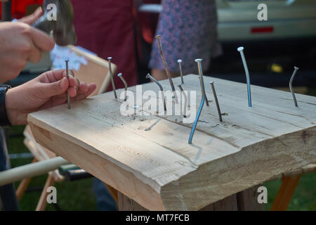 Man hammering a nail into a block of very hard wood which has caused several other nails to bend in a close up of his hands Stock Photo
