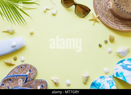 Traveler accessories: green tropical palm leaf, flip-flops, swimsuit, seashells and sunglasses are on yellow background with copy-space. Top view trav Stock Photo