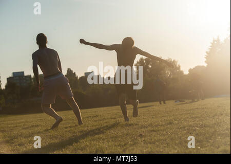 Two boys playing football with a dog in a London park, the pet keen to play too Stock Photo