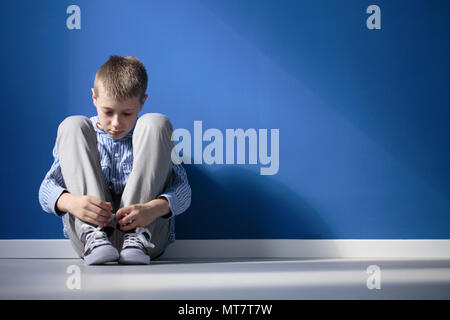 Depressed boy sitting on a floor in blue room Stock Photo
