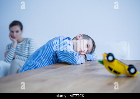 Depressed boy and his sad mom in a room with wooden table Stock Photo