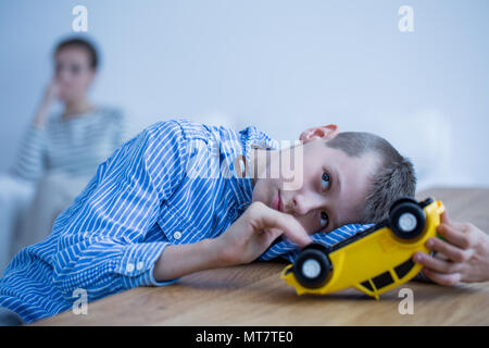 Sad autistic boy playing with toy car on wooden table