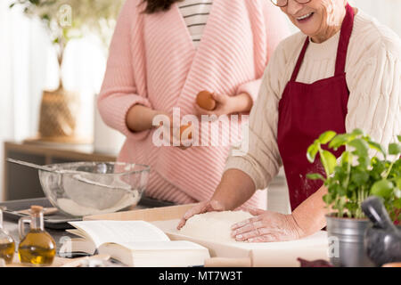 Happy grandma preparing a dough and her granddaughter helping her Stock Photo