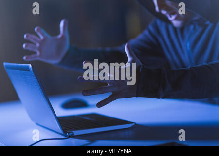 angry hacker with laptop shouting in dark room Stock Photo