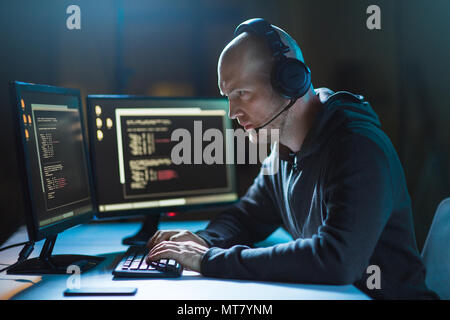 hacker with computer and headset in dark room Stock Photo