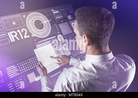 Calm young man holding a futuristic tablet and checking the information Stock Photo