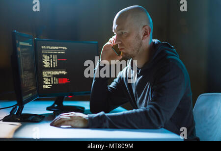 hacker with program on computer calling on cell Stock Photo