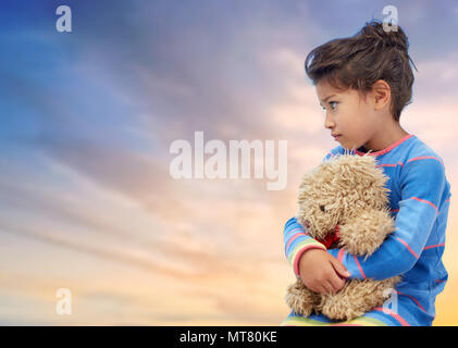 sad little girl with teddy bear over evening sky Stock Photo