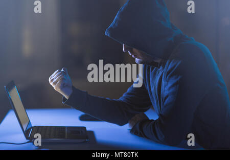 hacker showing fist to laptop in dark room Stock Photo