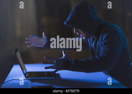 angry hacker with laptop computer in dark room Stock Photo
