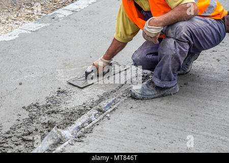 Worker leveling concrete with trowel, hands spreading poured concrete. Stock Photo