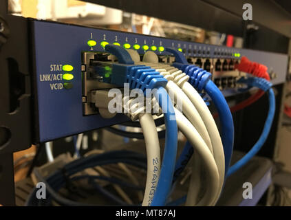 Blue white and orange networking cable hang out on the front of a hotel communications server rack Stock Photo