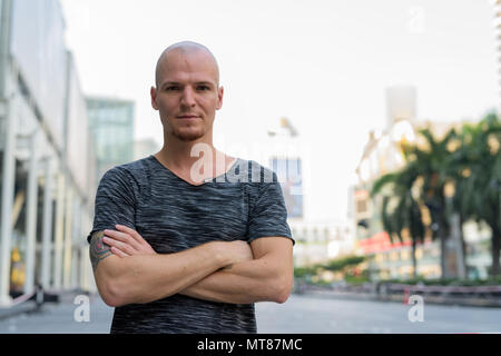 Young handsome bald man with arms crossed outside of the mall in Stock Photo