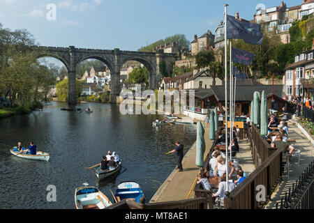 Blue sky & people relaxing by bridge at riverside cafe & boating in rowing boats on River Nidd  - scenic sunny summer day, Knaresborough, England, UK. Stock Photo