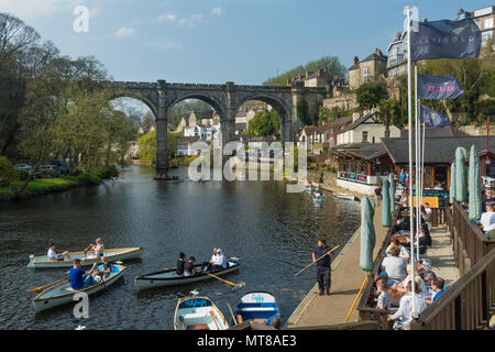 Blue sky & people relaxing by bridge at riverside cafe & boating in rowing boats on River Nidd  - scenic sunny summer day, Knaresborough, England, UK. Stock Photo