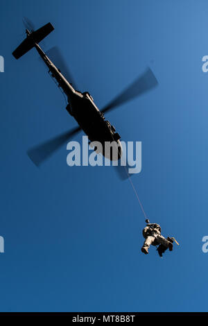 A Blackhawk helicopter winches up Spc. Claire Johnson, a flight medic with 3rd Battalion, 126th Aviation Regiment, D.C. Army National Guard in the field during a MEDEVAC exercise in Orono, Maine. The 126th Aviation Regiment is the only MEDEVAC support unit in the state and helps organizations from the Warden Service to Acadia National Park. Stock Photo