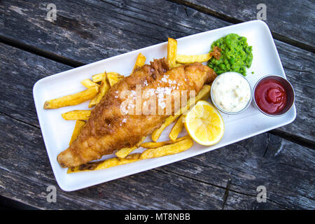 Plate of breaded fish and chips with mushy peas and tartar sauce served on a wooden table Stock Photo