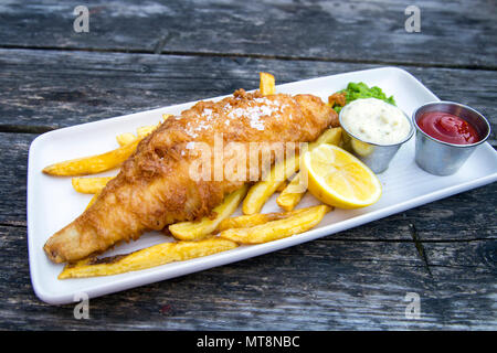 Plate of breaded fish and chips with mushy peas and tartar sauce served on a wooden table Stock Photo
