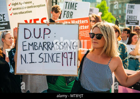 Belfast, Northern Ireland. 28/05/2018 - A woman holds a placard with the message 'DUP [Democratic Unionist Party].  Embarrassing NI [Northern Ireland] sine 1971'.  Around 500 people gather at Belfast City Hall to call for the decriminalisation of abortion in Northern Ireland.  It comes the day after a referendum held in the Republic of Ireland returned a substantial 'Yes' to removing the 8th amendment to the constitution, which gives equal right of life to both the mother and baby, effectively banning abortion in all circumstances. Stock Photo