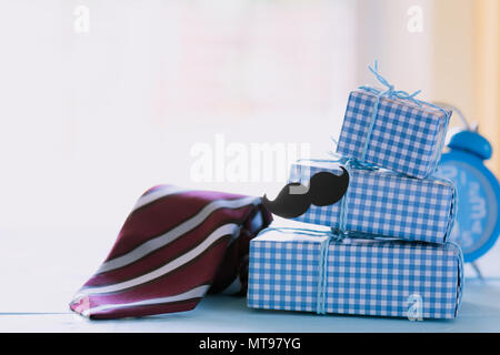 Happy fathers day concept. Stack of beautiful gift box with Red tie, blue alarm clock and mustache paper on bright blue pastel wooden table background Stock Photo
