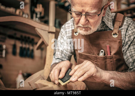 carpenter engaged in polishing an unfinished chair Stock Photo