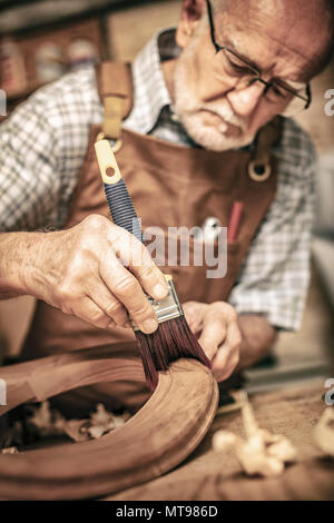 elderly carpenter uses a brush on an unfinished chair Stock Photo