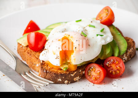 Healthy whole grain bread toast with avocado, poached egg, cherry tomato and baby leaves salad Stock Photo