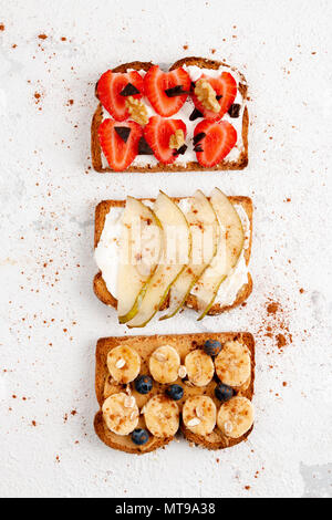 Assortment of healthy fruit toasts with strawberry, banana, pear, blackberries, with cheese cream, peanut butter, honey, cinnamon, chocolate, nuts and Stock Photo