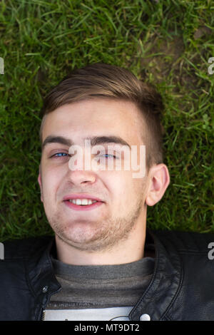 Head shot of a young man lying on grass and smiling. Close up. Portrait. Overhead shot. Stock Photo
