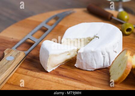 Soft cheese with white rind (camembert or brie) on wooden board with roasted bread slices, olives and white wine Stock Photo