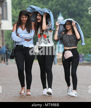 People using their jackets to shelter from a rain shower in Alexandra Palace, London. Stock Photo