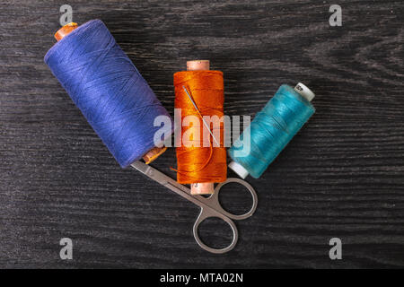 colored threads and scissors on a black wooden background Stock Photo