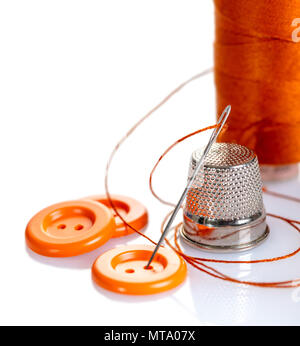 Needle with orange thread and buttons on a white background Stock Photo
