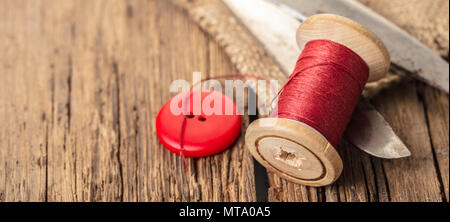 red thread with buttons and scissors, wooden background Stock Photo
