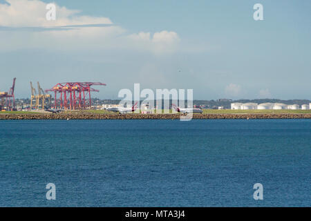 Two aeroplanes on the runway at Sydney Airport with Botany Bay in the foreground and cranes behind Stock Photo
