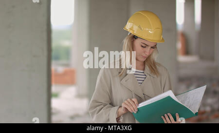 Young female architect construction engineer at a construction site eximaining documents Stock Photo