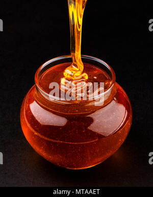 Pot of pouring honey on black background Stock Photo