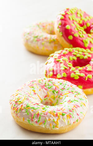 Sweet sprinkled donuts on white kitchen table. Stock Photo