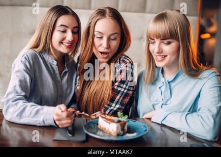 Three smiling chicks eats sweet cakes in cafe. Chocolate dessert and alcohol on the table Stock Photo